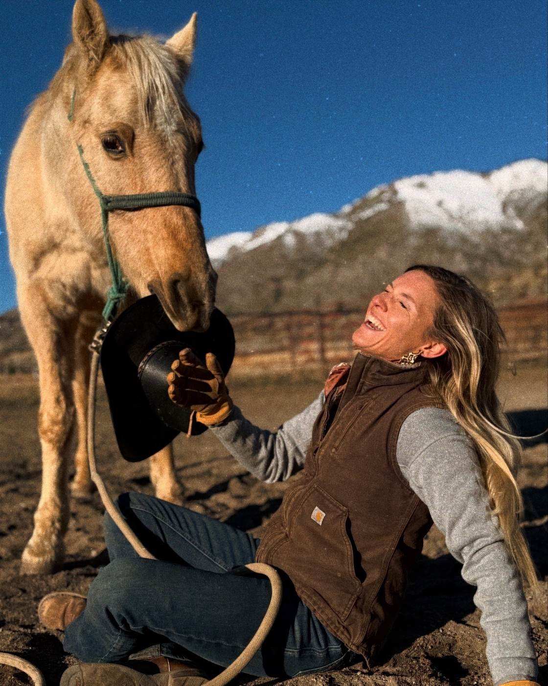 Outrider's founder sitting in the dirt laughing while her palomino takes her hat