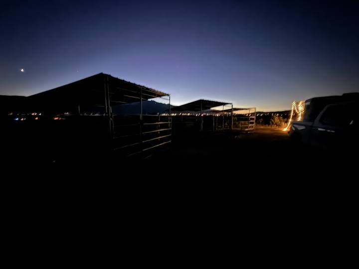 Covered horse pens at dusk, string lights on a rig beside them