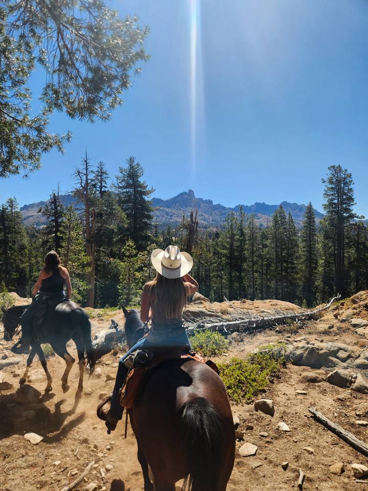 Two riders heading out through the pines toward a rocky peak